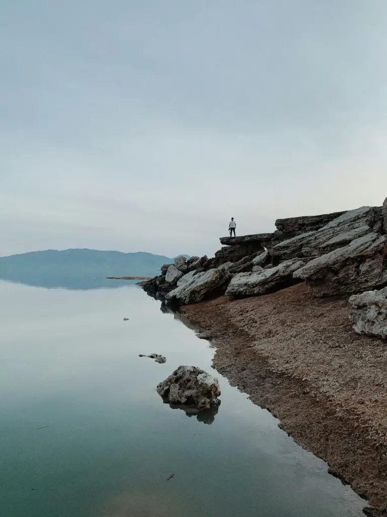 how do sedimentary rocks form on earth’s surface - A person standing on sedimentary rocks at the edge of a lake